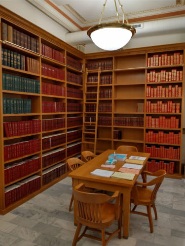 Picture of the new library space, featuring a work table and wooden shelving, a ladder, and research books.